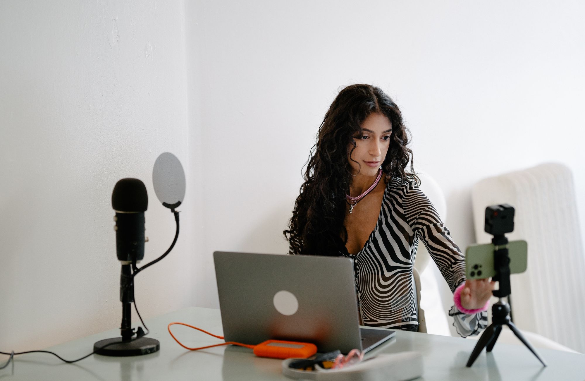 A seller at a laptop with a microphone and a phone on a tripod, set up to stream and record
